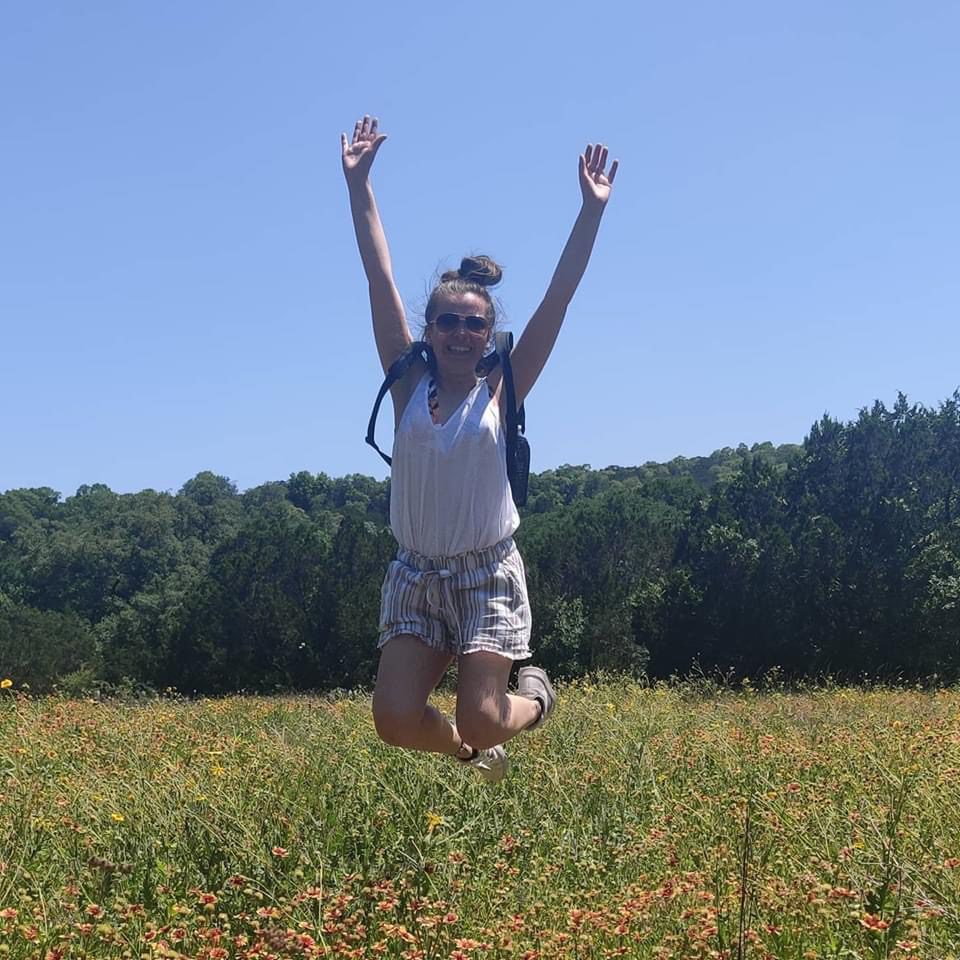 Person jumping in a sunny flower field.