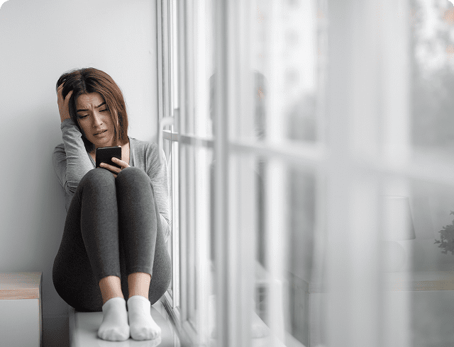 Woman sitting by window, looking at phone.