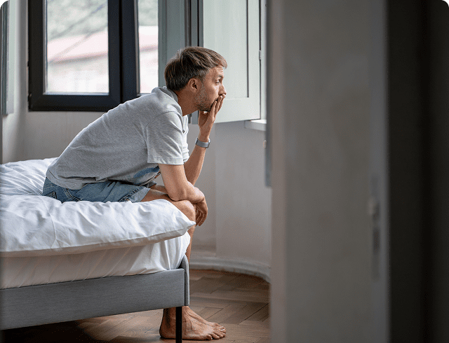 Man sitting on bed, looking pensive.