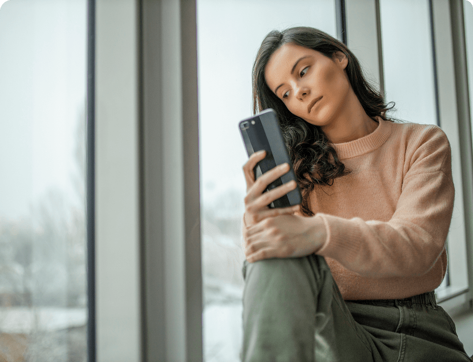 Woman sitting by window, looking at phone.