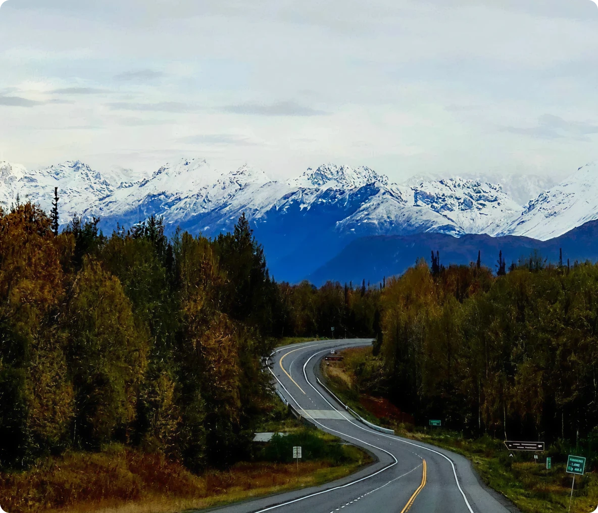 Mountain road with snow-capped peaks ahead.