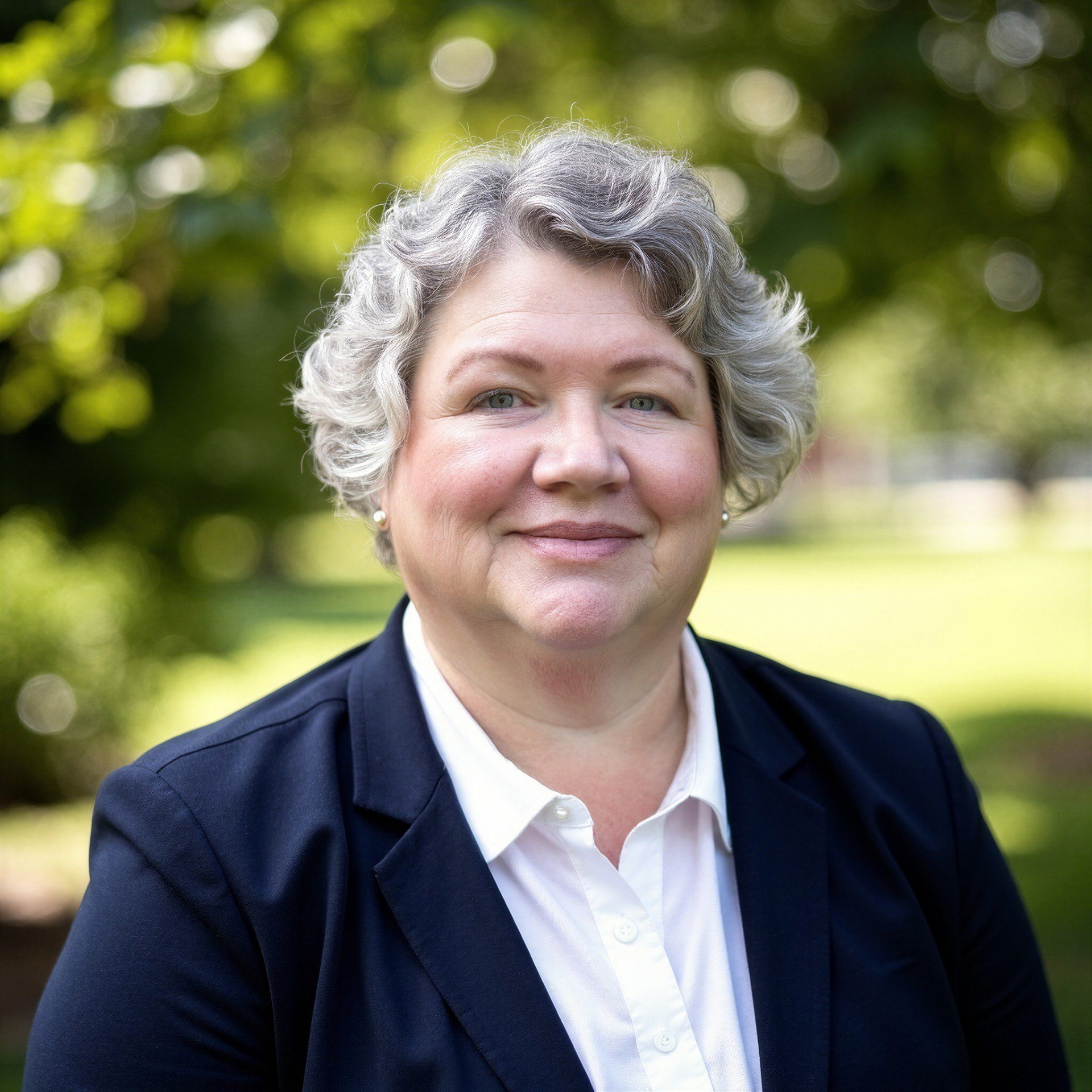 Smiling middle-aged woman with curly gray hair outdoors.